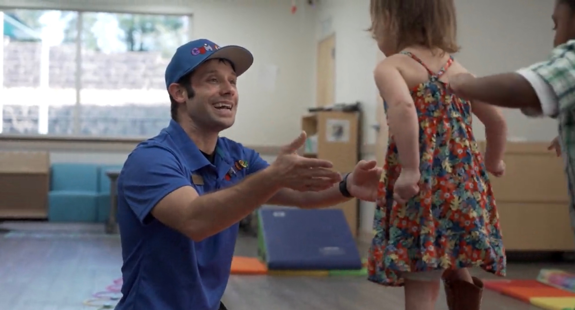 A smiling Gymplex coach encouraging a preschool child during an activity