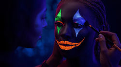 Fotografía editorial realista de un maquillador(a) aplicando maquillaje neón Lumins en un