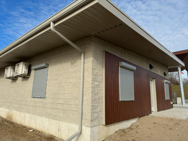 Corner view of public washroom building with multiple closed exterior roll shutters over window openings