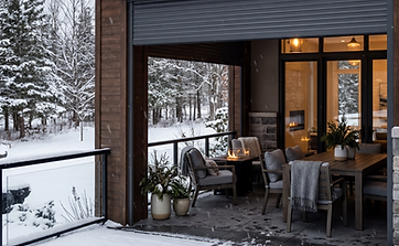 Enclosed pergola attached to home with roof overhang and two large roll shutters closing off the sitting area for seasonal weather and wind protection