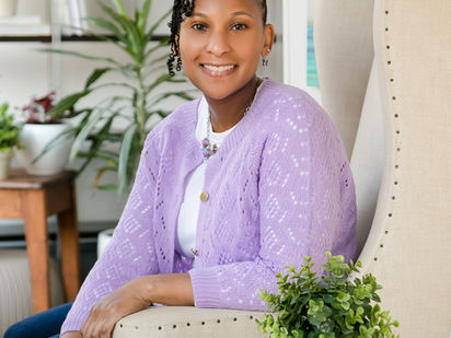 Woman sitting in a white chair wearing a white shirt and purple sweater.