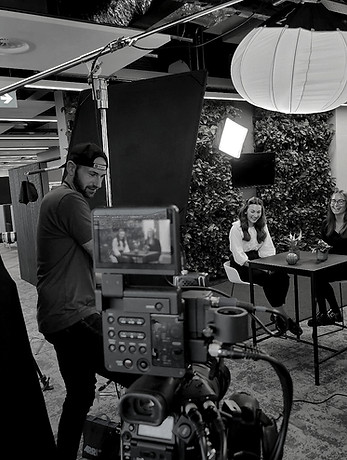 A black and white photo of a 'behind the scenes' photo of a camera pointing at a subject