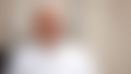 Smiling pope in white papal robes and skullcap against a soft beige background, looking calm and warm