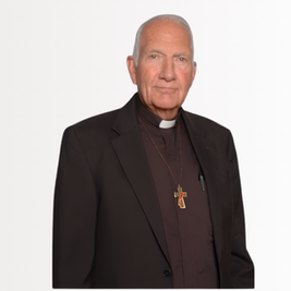 Elderly deacon in black clerical suit with cross pendant stands against a plain white background, looking calmly at the camera.