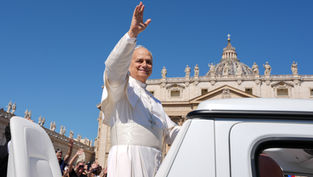 Pope in white waves from an open vehicle outside St. Peter’s Basilica as crowds cheer under a clear blue sky.