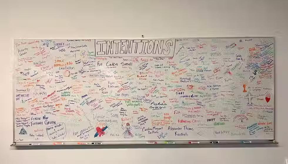 A whiteboard is covered in prayer intentions in different colored markers.