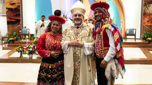 Smiling trio in colorful traditional dress pose inside a church altar; banners read Thanks to the LORD.