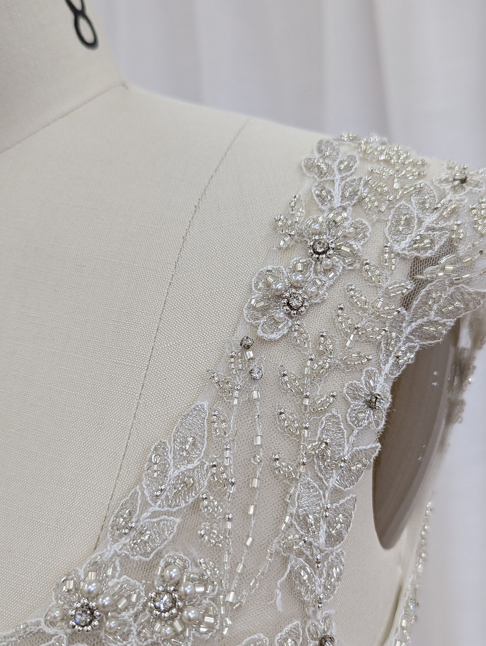 Thumbnail: Close-up of the Caitlyn gown’s bodice, highlighting intricate silver and pearl beadwork on sheer tulle with delicate cap slee