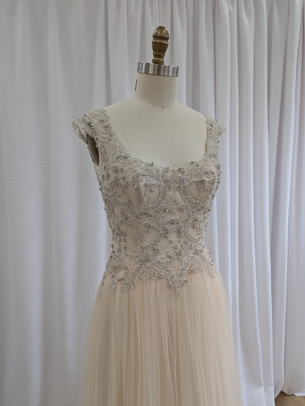 The Maggie Sottero Caitlyn gown on a mannequin, showing the Light Gold/Pewter beaded bodice and champagne tulle skirt.bodice