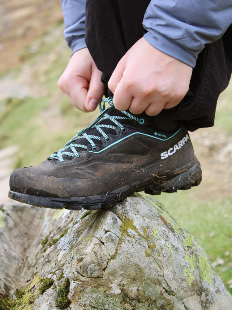 Hands tying laces of walking boot balanced on rock.