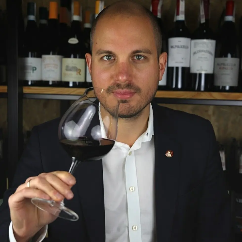 Studio photography of a sommelier holding a glass of red wine. He is in front of wine shelves, conveying a professional and sophisticated atmosphere.