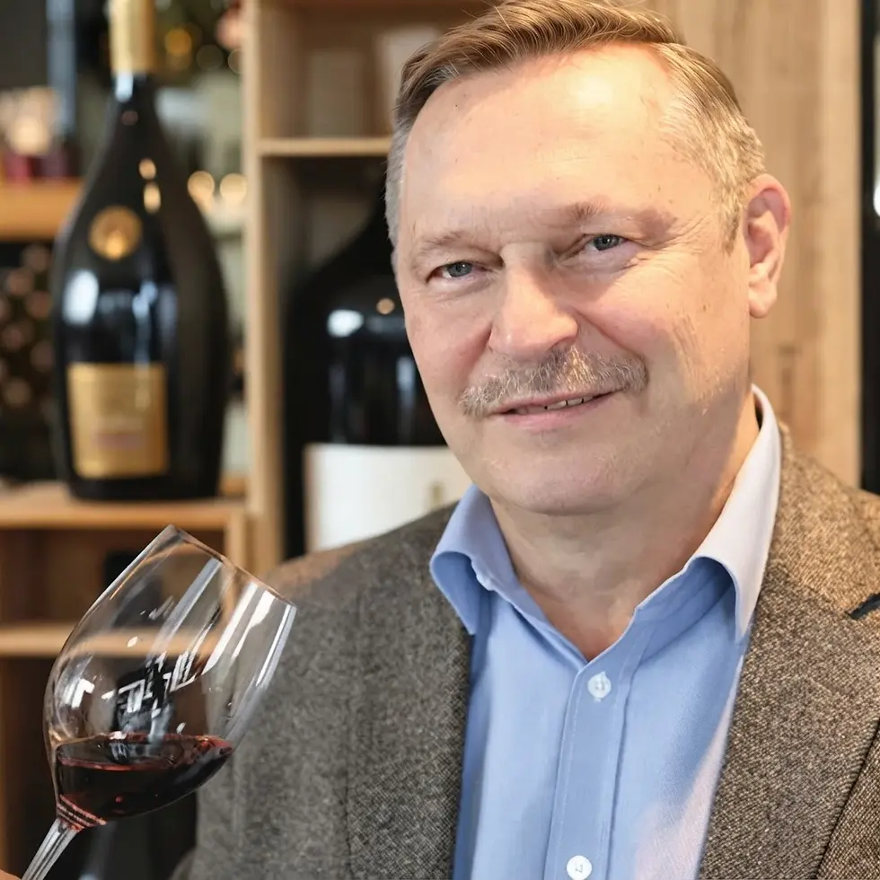 Packshot photography of a man holding a glass of red wine. He is in a wine shop with bottles of wine displayed in the background.