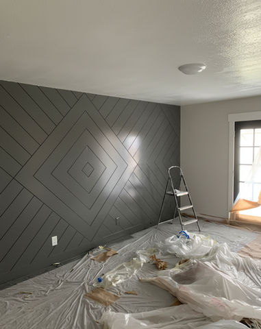 Grey geometric accent wall, ladder, and covered floor during renovation project.
