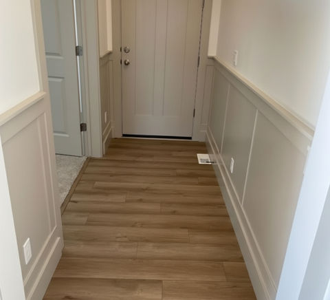 Hallway with wooden floor and white door leading into the home.