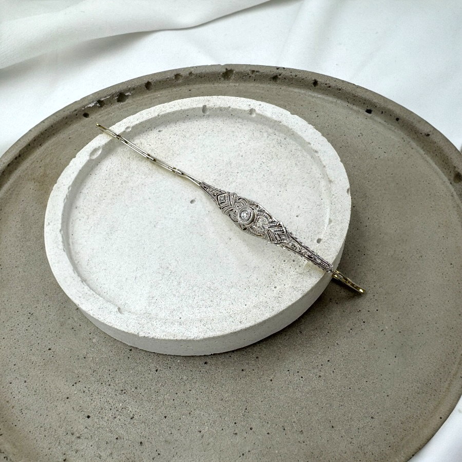 Elegancka bransoletka w stylu art déco z białego i żółtego złota, ułożona na dekoracyjnej, jasnoszarej podstawce.