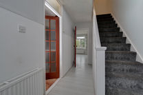 Hallway with stairs and open door, leading to room.