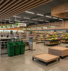 Interior de supermercado reformado, setor de hortifruti com prateleiras de frutas e verduras, forro ripado em madeira e luminárias pendentes geométricas