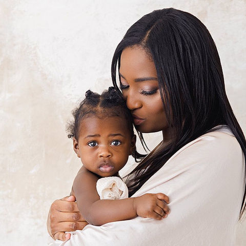 Mother holds 5 month old daughter and kisses her in front of photography backdrop