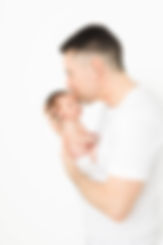 Father stands in white studio and kisses newborn boy in his hands
