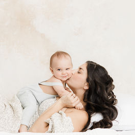 Mother lies on back kissing 4 month old daughter 