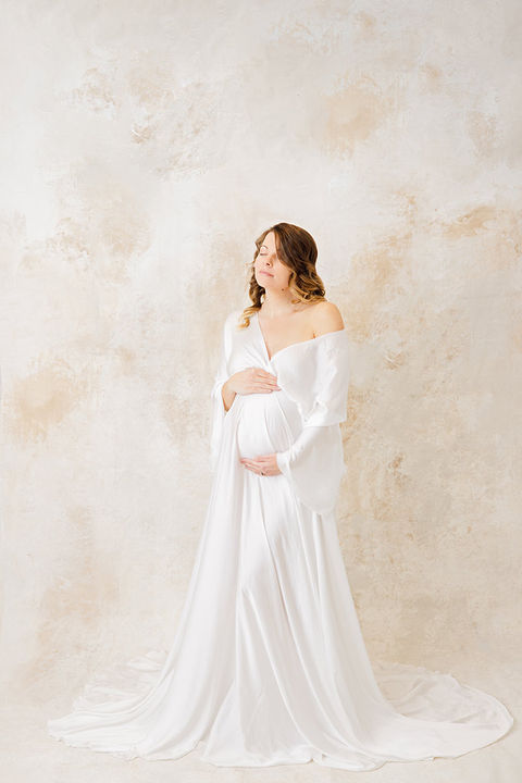 Pregnant woman in gown embracing belly.