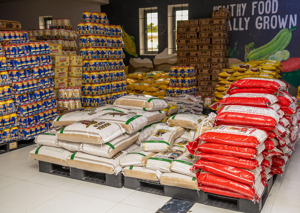 Stacks of semo and flour in red and white packaging, canned goods, and other food items in a Betty Distribution Depot. Background shows a mural and text "HEALTHY FOOD."