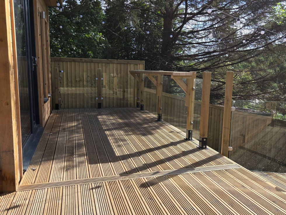 Timber deck with glass balustrade and festoon lighting beside the garden room bar, Cumbria
