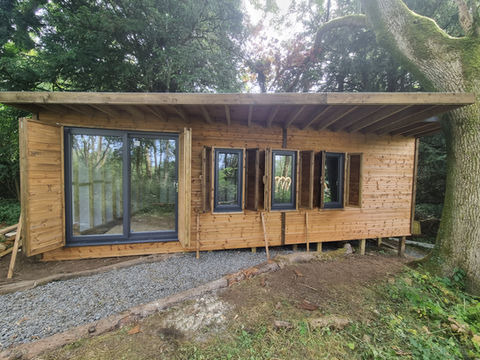 Woodland studio cabin with large sliding glass doors and open shutters in natural timber cladding