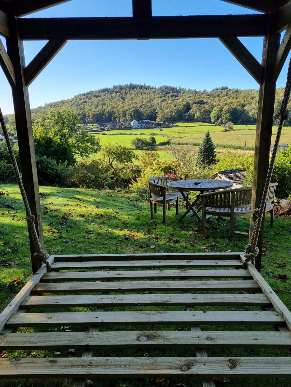 View through the swing bed frame overlooking a countryside garden and patio seating