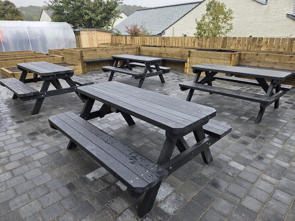 composite picnic tables on paving with timber raised beds and polytunnel, Cumbria community garden