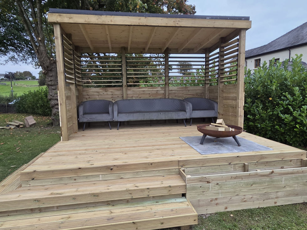 Open-front timber garden shelter with three grey sofas and a corten firepit, Cumbria