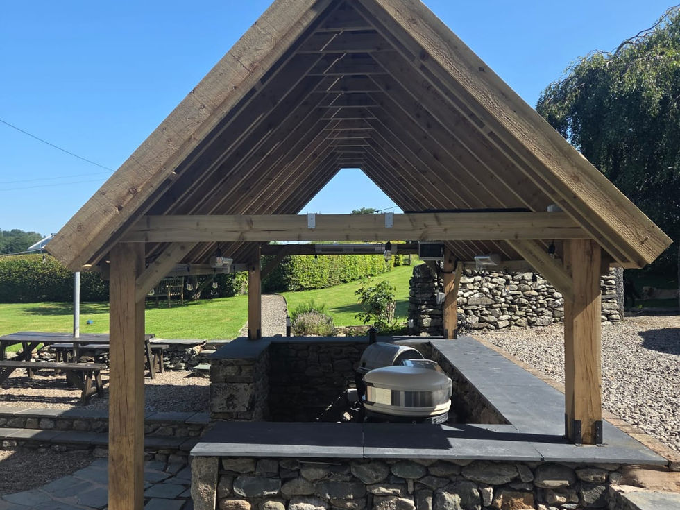 Dramatic asymmetric offset-ridge roofline over a Gozney pizza oven and slate worktop, Cumbria