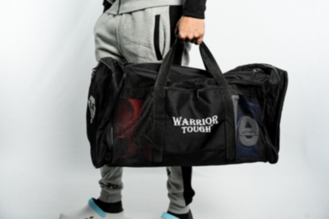 Person holding a black WT Mesh Gym Bag with Warrior Tough on it.