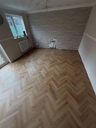 A room with new herringbone-patterned wooden flooring, light gray textured wallpaper, and a radiator under large windows. Bright and modern tone