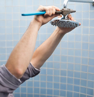 A man uses a wrench to fix a showerhead against a blue tiled wall