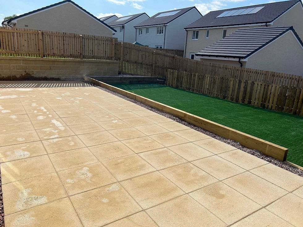 A backyard with a large beige tiled patio in the foreground