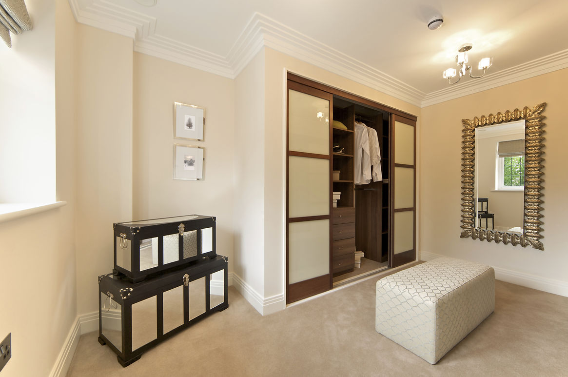 Spacious room with an open wardrobe showing clothing, a large ornate mirror, stacked decorative boxes, and a quilted bench