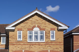 Brick house with a gable roof section, featuring three white-framed windows against a clear blue sky and a small cloud