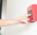 A man points at a fire alarm mounted on a wall
