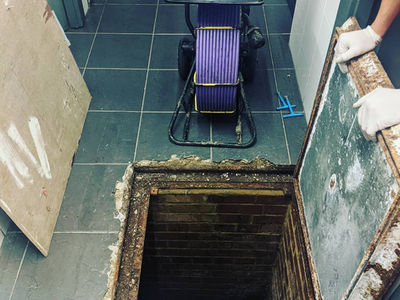 An indoor tiled floor with an open recessed manhole hatch showing a portable survey reel nearby