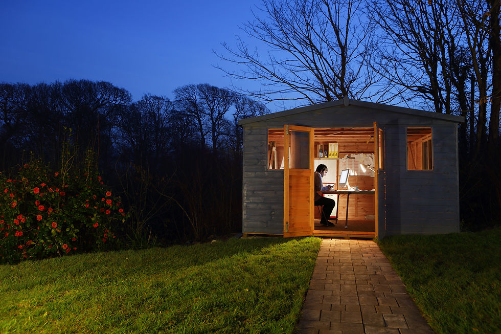Cozy wooden garden office shed illuminated at dusk with a person working inside at a computer desk