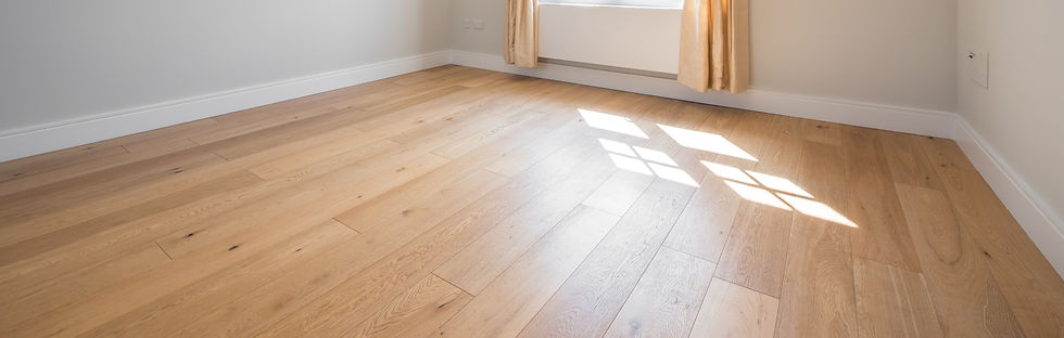 Sunlit empty room with light wooden flooring, cream walls, and a white-framed window