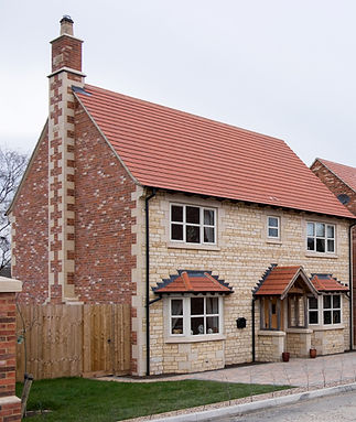 Two-story house with red-tiled roof, a mix of brick and stone exterior, white-framed windows, and a wooden door