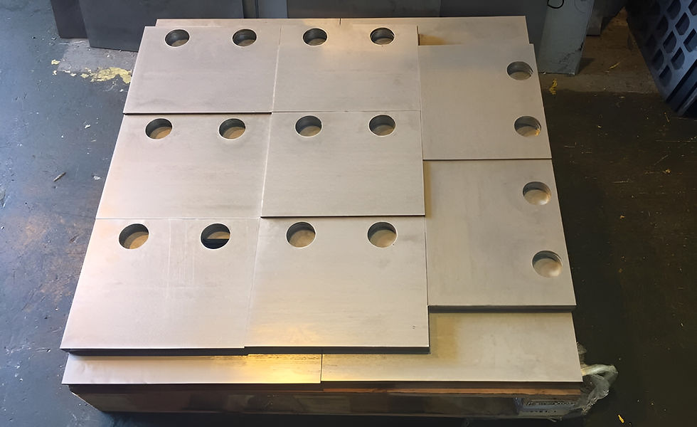 Square laser-cut steel plates with circular cutouts stacked on a wooden pallet inside a metal fabrication facility