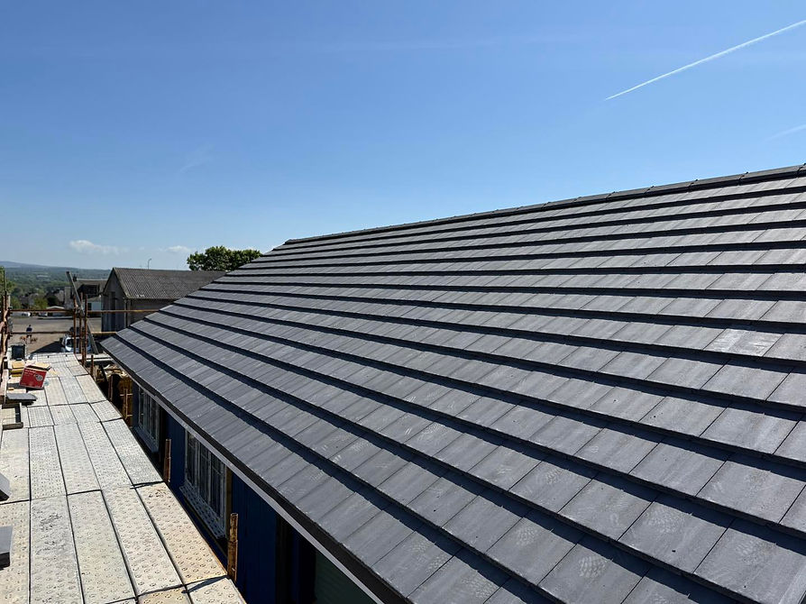 A new slate roof under clear blue sky, partially covering scaffolding and construction area