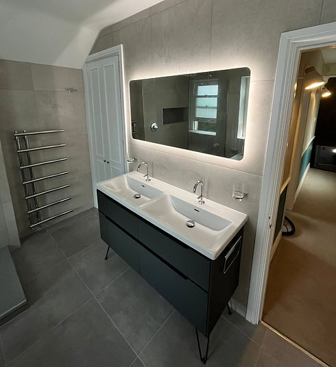 Modern bathroom corner featuring a back-to-wall freestanding bathtub with matte black fixtures and large neutral grey tiles