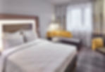 Modern hotel room with a neatly made bed, white linens, and illuminated wooden headboard