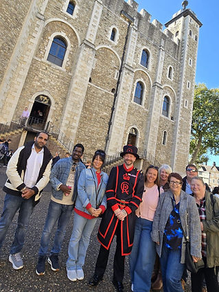 A group of nine people stands smiling in front of the Tower of London on a sunny day