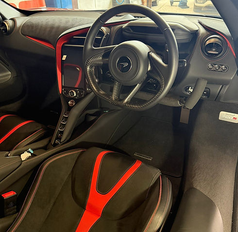 Close up of a leather steering wheel fitted with bespoke driving hand controls inside a luxury car cockpit