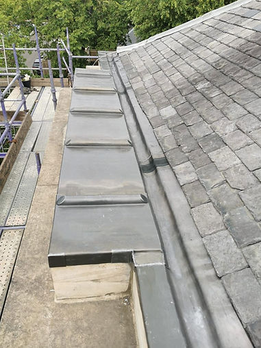 Pitched slate roof with freshly installed lead flashing, parapet capping, and lead valley gutter beside scaffolding